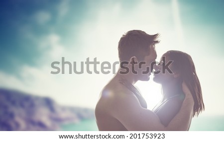 Silhouettes of the head and shoulders of a romantic young couple kissing backlit by the sun with a coastal backdrop