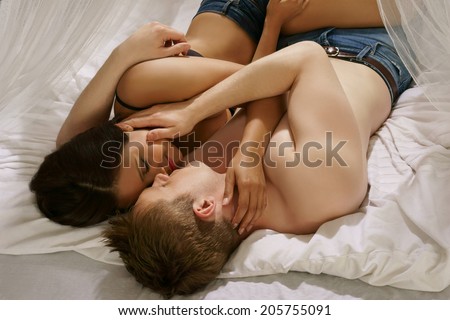 Romantic couple having a kiss and cuddle in bed lying entwined in each others arms lovingly caressing each other with their heads towards the camera