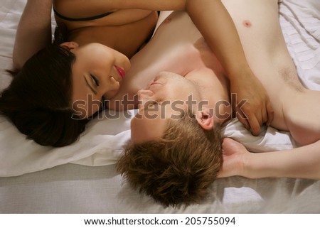 Romantic naked couple relaxing in bed lying side by side looking lovingly at each other with their heads towards the camera