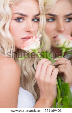 Gorgeous blond woman with blue eyes reflected in a mirror holding a single pink rose to her lips symbolic of love and romance