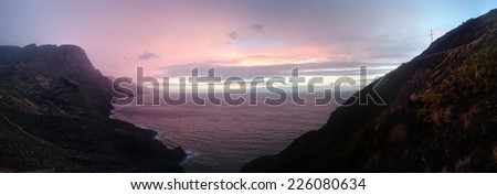 Colorful panoramic sunset or sunrise over a tranquil ocean and coastline on a cloudy day viewed from a headland or mountain peak