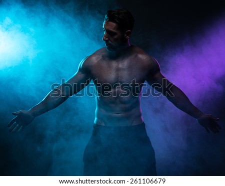 Portrait of a Silhouette Shirtless Muscled Man Posing in the Smoke and Looking at the Camera on a Dark Blue Green Background.