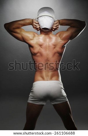 Portrait of a Sexy Topless Athletic Man Showing his Back Muscles with Tattoo on a Gray Background.