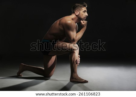 Portrait of a Topless Muscular Man Sitting on the Floor in a Yoga Position Looking at the Camera on a Black Background.