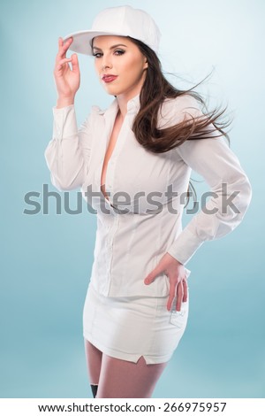 Half Body Shot of a Pretty Long Hair Woman, Posing in White Fashion with Cap, Showing Sexy Cleavage While Looking at the Camera on a Very Light Blue Background