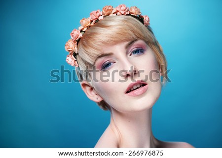 Gorgeous sensual blond woman wearing a headband of small pink roses looking at the camera with a sultry sensual expression over a blue background
