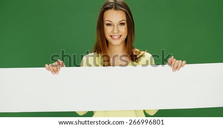 Smiling woman holding a long blank white horizontal banner in her hands looking over the top with a friendly smile, over green