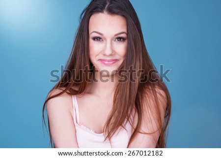 Gorgeous laughing playful young woman with a beaming smile looking to the right of the frame, head and shoulders over blue