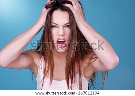 Attractive young woman throwing a temper tantrum tearing at her hair and yelling in rage and frustration, close up of her face