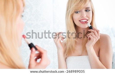 Young Smiling Blond Woman Looking Into Mirror and Applying Lipstick, Getting Ready to Go Out