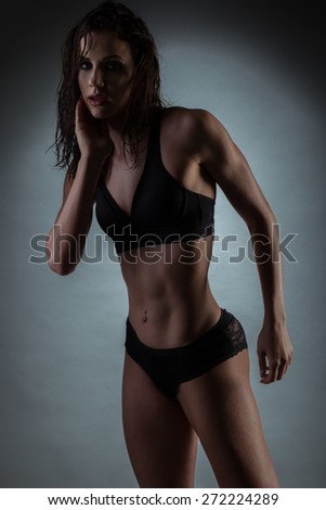 Portrait of a Seductive Gym Fit Woman, Wearing Black Underwear, Touching her Face While Looking at the Camera. Captured in Studio with Gray Gradient Background.