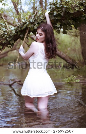 Brunette Woman Wearing Short White Sun Dress Standing Thigh Deep in Water Holding Onto Tree Branch and Looking Virginal and Seductively Back Over Shoulder