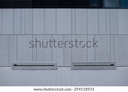 Two Empty Similar Benches Against White Building Wall with Vertical Line Orientation.