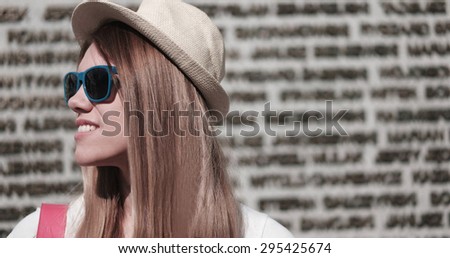 Close up Stylish Young Pretty Woman Wearing Hat and Sunglasses, Looking to the Left of the Frame Against Concrete Building Wall.