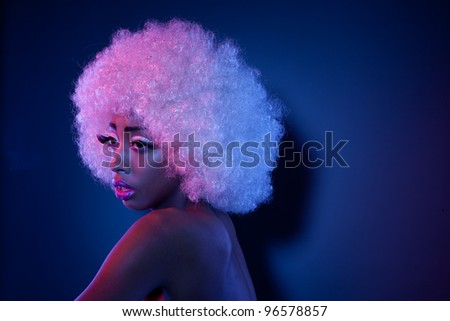 Attractive African model in creative makeup and a large curly white Afro style wig looking out of frame with copyspace behind.