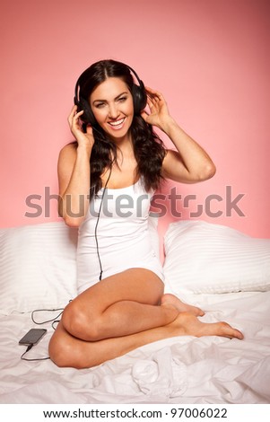 Vivacious woman curled up on her bed wearing headphones and listening to music