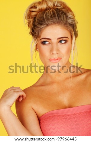 woman in a pink tube top, blonde hair in an up-do, with a wondering expression, lips slightly pursed, her right hand touching her right shoulder, eyes looking to her right, with yellow background
