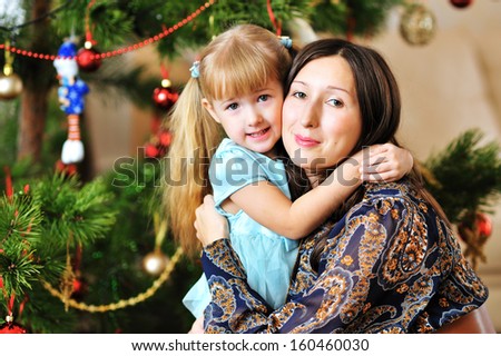 Happy young mother and her daughter hugging near Christmas tree.