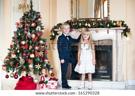 Happy brother and sister standing near the fireplace and a Christmas tree. children waiting for the new year