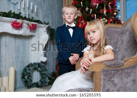 Happy sister sitting in a armchair and brother standing near. little friends enjoying New Year party, Christmastime holidays, best friends, happiness concept