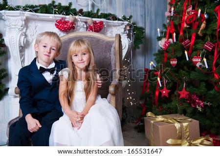Happy brother and sister are sitting embracing near Christmas tree. little friends enjoying New Year party, Christmastime holidays, best friends, happiness concept