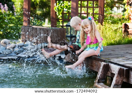 brother and sister sitting on the wooden bridge and dangling  legs in the water