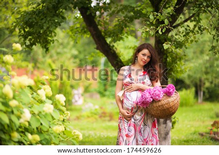 portrait of pregnant beautiful woman with hands over tummy with a basket of flowers in the park in summer