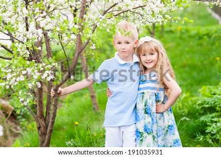 portrait of happy brother and sister hugging near flowering tree in a warm spring day