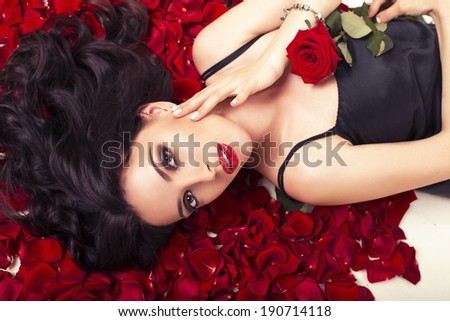 beautiful sexy woman with dark curly hair lying on the petals of roses