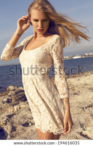beautiful girl with blond hair in elegant lace dress posing beside a sea