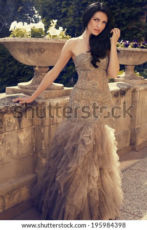 beautiful woman with black hair in luxurious sequin dress posing at summer park