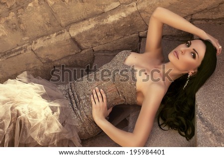 sexy beautiful woman with black hair in elegant beige dress lying on stairs at park