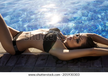 fashion photo of sexy beautiful girl with long wet hair in black bikini relaxing beside a swimming pool
