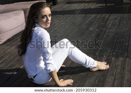 fashion photo of sexy glamour model with long wet hair in white shirt and pants sitting on wood floor
