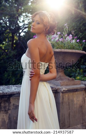 tender photo of beautiful bride in elegant dress posing at park in sunlight rays