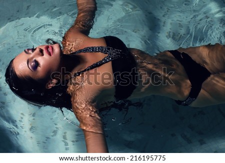 fashion photo of sexy beautiful girl with dark hair posing in swimming pool at night