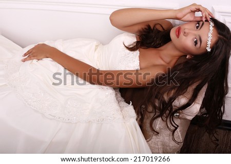 fashion photo of beautiful young bride with long dark hair in elegant wedding dress posing at studio