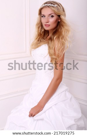 fashion photo of beautiful bride with long blond hair in elegant dress and diadem posing at studio