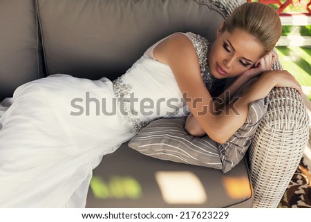 fashion photo of beautiful bride with blond hair in elegant wedding dress relaxing on divan