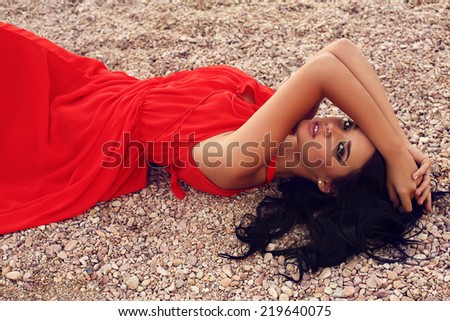 fashion outdoor photo of sensual beautiful woman with dark hair in elegant red dress posing on beach