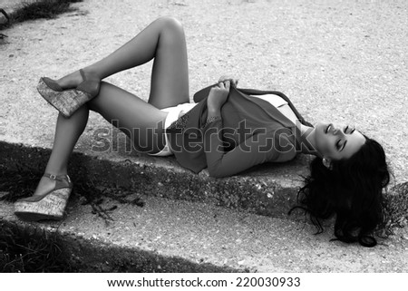 black and white fashion photo of sexy woman with dark hair in elegant jacket and shoes lying on stairs
