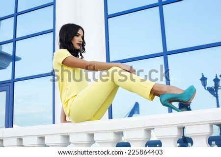 fashion outdoor photo of beautiful glamour woman with dark hair wearing elegant yellow suit and blue shoes
