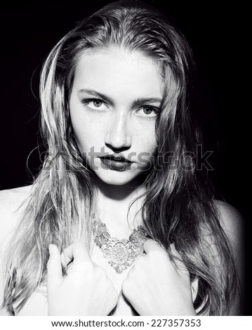 fashion black and white portrait of beautiful girl with blond hair and freckles posing at dark studio