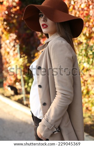 fashion outdoor photo of beautiful elegant ladylike woman with dark hair wearing coat and felt hat,posing in autumn park