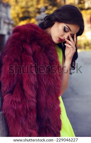 fashion outdoor photo of beautiful elegant woman with dark hair wearing luxurious red fur coat,posing in autumn park