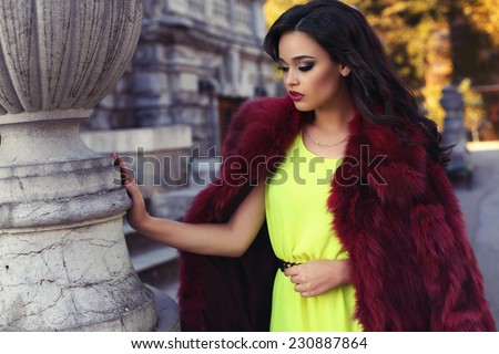 fashion outdoor photo of beautiful elegant woman with dark hair wearing luxurious red fur coat and bright dress,posing in old castle