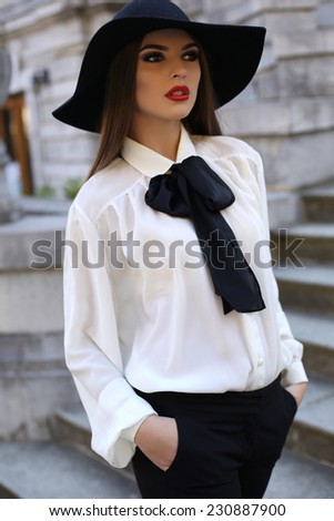 fashion outdoor photo of beautiful girl with dark hair and bright makeup,wearing elegant blouse and black hat,posing on stairs in autumn park