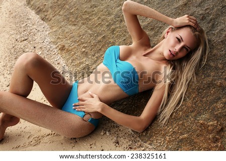fashion photo of sexy beautiful woman with blond wet hair in elegant blue swimsuit relaxing on sand