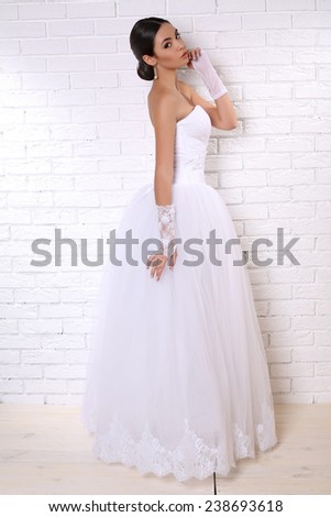 fashion studio photo of beautiful young bride with dark hair in elegant wedding dress and lace gloves