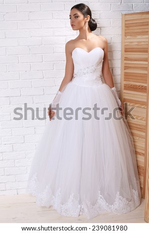 fashion studio photo of beautiful young bride with dark hair in elegant wedding dress and lace gloves